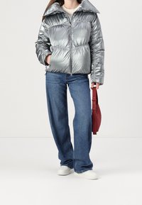Metallic silver puffer jacket with a high collar, zip closure, and elastic waist. Paired with blue wide-leg jeans and white sneakers.
