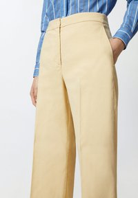 Svijetlosmeđi široki hlače od ugodne tkanine, s visokim pojasom i bočnim džepovima, u kombinaciji s plavom majicom na pruge.