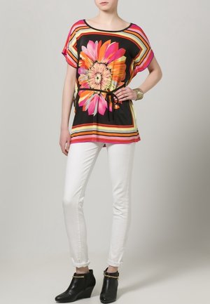 Czarna bluzka w kwiaty w kolorach różowym, żółtym i pomarańczowym, z elastycznym ściągaczem w talii. Połączona z białymi obcisłymi spodniami i czarnymi botkami za kostkę.