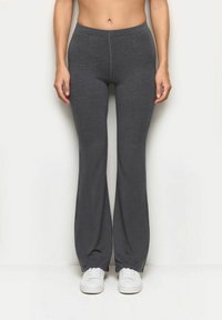 Szare, elastyczne spodnie z rozszerzanymi nogawkami i elastycznym pasem, z gładką teksturą i czystym szwem z przodu. Białe sneakersy na dole.