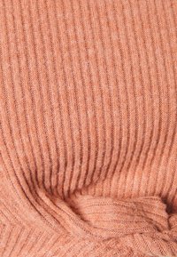 Stickad tyg i mjuk persikofärg, med vertikal ribbad textur, lätt fluffighet och en strukturerad utseende.