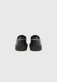Baskets plateformes noires avec un dessus en cuir lisse, semelle nervurée et détail de marque au dos. Présentent un nez arrondi et une languette pour un enfilage facile.