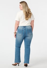 Jean en denim bleu clair avec une coupe droite, taille haute et deux poches arrière. Un haut crème à manches courtes complète la tenue.