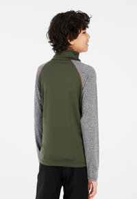 Langarmtop met een hoge kraag, groene body, grijze mouwen en contrasterende rode stiksel langs de schouders. Zachte, текстурierte stof.