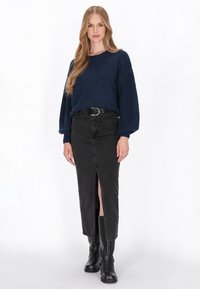 Pullover bleumarin tricotat cu mâneci largi, asortat cu o fustă din denim neagră cu fante adânci. Botine negre până la gleznă completează ținuta.
