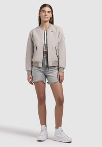 Helebeež bomber-jakk ribatud mansettide, musta tõmbluku ja kahe ees oleva taskuga, kombineerituna hallide teksashortside ja valgete kõrgete tennisetossudega.