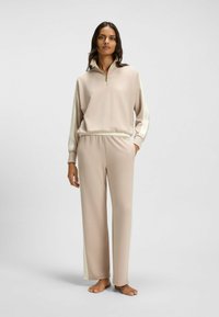 Maglione beige con zip a quarto di giro e dettagli a strisce laterali, abbinato a pantaloni palazzo coordinati. Tessuto morbido, vestibilità rilassata.