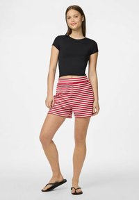 Melna īsām piedurknēm veidota cropped topa, kas saskaņota ar sarkaniem un baltiem svītrainiem šortiem. Apģērbs ir ar vienkāršu dizainu un brīvu piegriezumu.