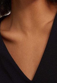 Zbliżenie na dekolt w ciemnym materiale, z subtelnym kształtem V. Kolor skóry widoczny wokół obszaru kołnierza, gładka tekstura i brak wzorów.