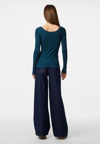 Teallfärgad långärmad topp med ribbstruktur och rundad rygg, tillsammans med vida mörk denimjeans med bakfickor och en avslappnad passform.