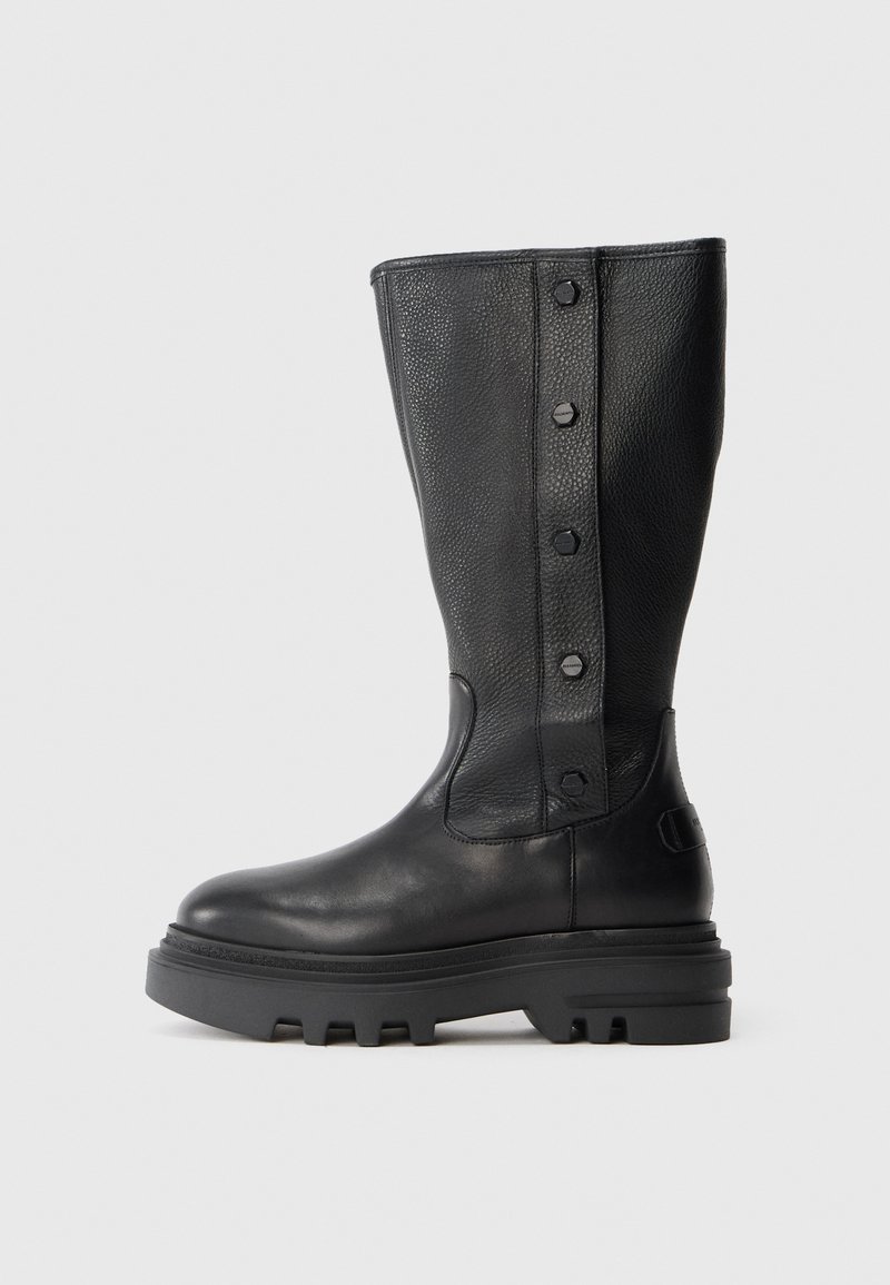 Bota de cuero negra hasta la rodilla con suela de goma gruesa y cuatro botones decorativos a lo largo del panel lateral texturizado.