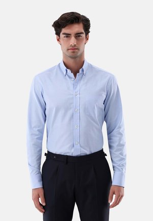 Camicia azzurro chiaro con un sottile motivo a quadri, maniche lunghe e taschino sul petto, abbinata a pantaloni scuri con vestibilità su misura.