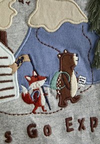 Hall hallide kangas, millel on puuderitud metsaelukate kujutised: punane rebane sauaga ja pruun karu seljakotiga, ümbritsetud looduse elementidega.