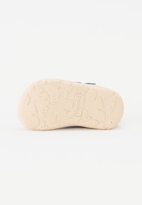 Sole de cauciuc de culoare deschisă, cu un model texturat și o gravură vizibilă a mărcii. Partea superioară netedă are o nuanță generală de albastru.