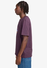 Purple cotton t-shirt with short sleeves, featuring a graphic design on the front. The fit is relaxed, paired with blue denim jeans.