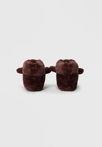 Brown plush slippers with a soft texture, rounded shape, and small side handles. The fabric features a smooth finish.