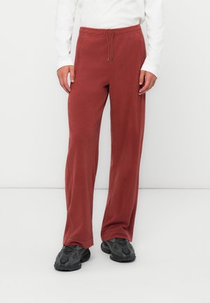 Pantaloni della tuta bordeaux con cintura regolabile, gamba larga e texture morbida. Abbinati a scarpe sportive nere. Design semplice e comodo.