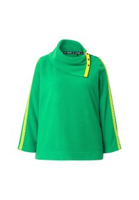 Top verde de manga larga con cuello de cisne. Presenta un detalle de botón amarillo y un patrón lateral en amarillo. Material suave con un ajuste relajado.