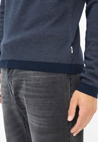 Maglione blu navy strutturato con orlo e polsini a coste, caratterizzato da un sottile motivo chiaro, abbinato a jeans grigio scuro.