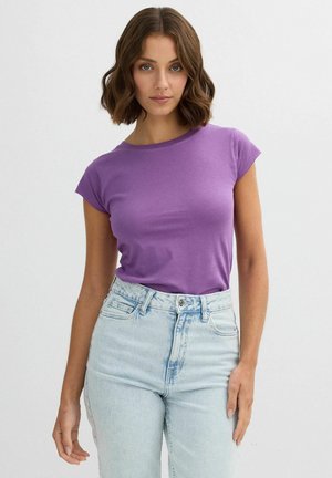 Camiseta morada de manga corta hecha de una tela suave, con un clásico escote redondo. Combinada con jeans de mezclilla de tiro alto en un tono azul claro.