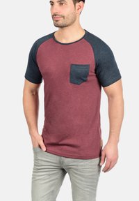 Short-sleeved t-shirt with a maroon body and dark blue raglan sleeves. Features a chest pocket and textured fabric.