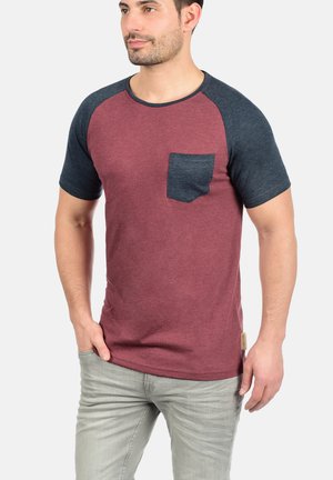 Short-sleeved t-shirt with a maroon body and dark blue raglan sleeves. Features a chest pocket and textured fabric.