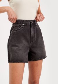 Hoge taille zwarte denim shorts met een vervaagde textuur, voorkzakken en contrasterende stiksels. Voorzien van een knoop- en ritssluiting.