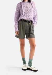 Lavendelfärgad stickad tröja med ett strukturerat mönster, kombinerad med svartvitrutiga shorts, svart bälte och gröna mönstrade strumpor med vita skor.