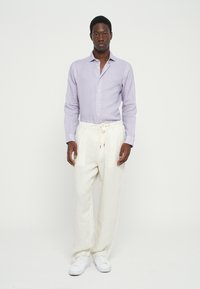 Chemise à manches longues boutonnée, de couleur violet clair et à motifs, assortie à un pantalon en lin blanc, décontracté et à coupe ample, ainsi qu'à des baskets blanches. Design et texture simples.