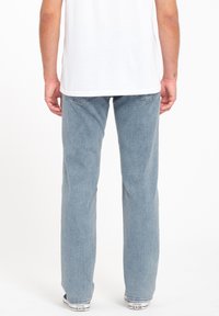 Jeans droits bleu clair avec une finition texturée, taille élastique et design à cinq poches, portés avec des baskets blanches.