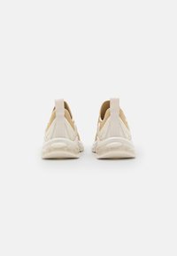 Baskets légères avec une tige crème, des accents marron clair, un design sans lacets et une semelle en caoutchouc transparente amortie. Dotées de languettes en tissu à l'arrière.