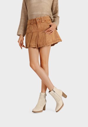 Mini gonna in suede tan con pieghe, abbinata a stivaletti crema con design perforato e tacco spesso.