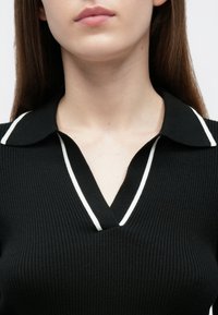 Top preto canelado estilo polo com decote em V com acabamento branco. Mangas curtas e tecido texturizado criam um visual ajustado.