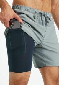 Herren Sport shorts mit einer hellgrauen Außenschicht und einem dunkelblauen Innenfutter, ausgestattet mit einer Seitentasche für ein Smartphone.