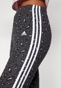 Šedé legíny s černým leopardím potiskem, s bílými bočními pruhy a logem Adidas na stehně. Elastický materiál, přiléhavý střih.