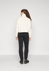 Afskåret, hvid sweatshirt med høj krave, kombineret med sorte, tætsiddende sweatpants og mørke sneakers. Glat stof med ribbede manchetter.