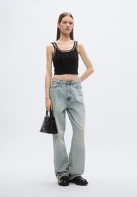 Juodas megztas trumpas viršus su plačiomis petnešėlėmis, šviesiai mėlynos aukšto liemens džinsai, juoda rankinė ir masyvūs juodi batai. Lygi tekstūra ir laisvas siluetas.