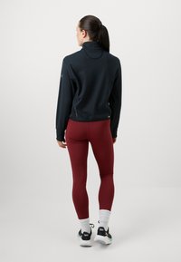 Črna športna jakna z visokim ovratnikom, kombinirana z oprijetimi bordo pajkicami. Jakna ima teksturirane vzorce. Bele nogavice in črni supergi.