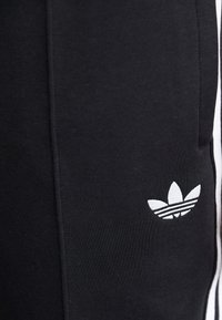 Black athletic pants made of smooth fabric, featuring a white embroidered three-stripe logo on the left thigh and side stripe detailing.