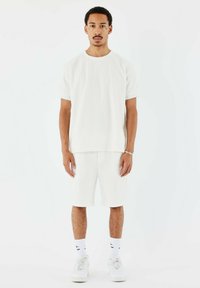 Camisa corta de manga corta texturizada blanca y pantalones cortos a juego, ambos hechos de material transpirable. Llevado con zapatillas blancas y calcetines.