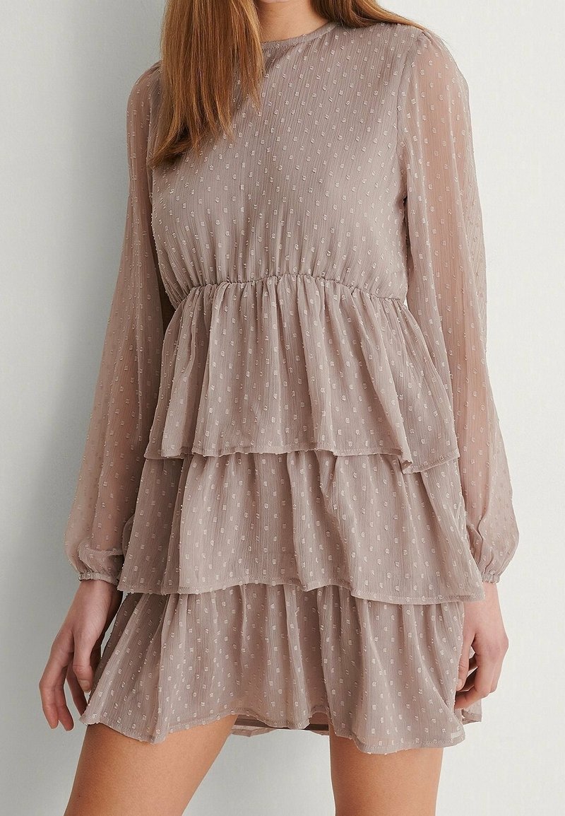 Robe mini beige à manches longues étagée avec des pois texturés, taille cintrée et tissu semi-transparent aux manches et aux couches.
