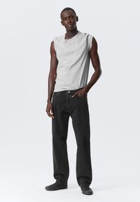 Gray sleeveless shirt with a soft texture, paired with loose black denim jeans featuring a button and zip closure. Black sneakers complete the outfit.
