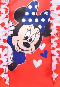 Tissu rouge avec un graphique de Minnie Mouse, un nœud à pois bleus et une bordure frisée blanche. Accentué de cœurs colorés en rose, bleu et argent.