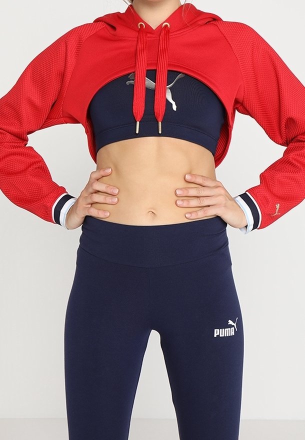 Rode cropped hoodie met mesh-structuur en trekkoorden, gecombineerd met een donkerblauwe sportbeha en marineblauwe legging met een wit logo.
