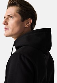 Czarna bluza z kapturem ze sznurkiem, dopasowany krój, miękka tekstura i widoczne detale szwów. Profil modela zaprezentowany na jasnym tle.