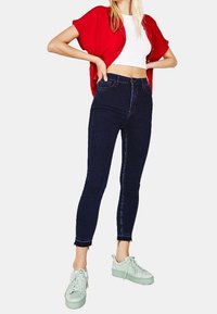 Korkeavyötäröiset tummansiniset skinny-farkut, joissa on revitty helma, yhdistetty valkoiseen crop-toppiin ja punaiseen lyhythihaiseen paitaan, sekä mintunvihreät tennarit.