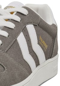 Gray suede sneaker with white leather stripes and golden logo. Features white laces and a textured rubber sole, offering a sporty design.