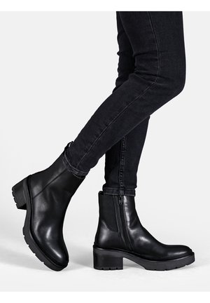 Sorte læder ankelstøvler med en kraftig hæl, sideskydelås og struktureret sål; båret med mørke skinny jeans.