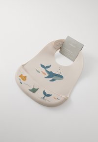 Silicone baby bib in soft beige with a rounded neck. Features marine-themed illustrations including a whale and fish, with smooth texture.