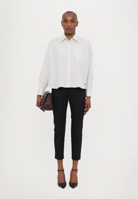 Witte gestreepte overhemd met een relaxte pasvorm, gecombineerd met slim-fit zwarte broek tot de enkel en een donkerbruine handtas. Zwarte hakken.